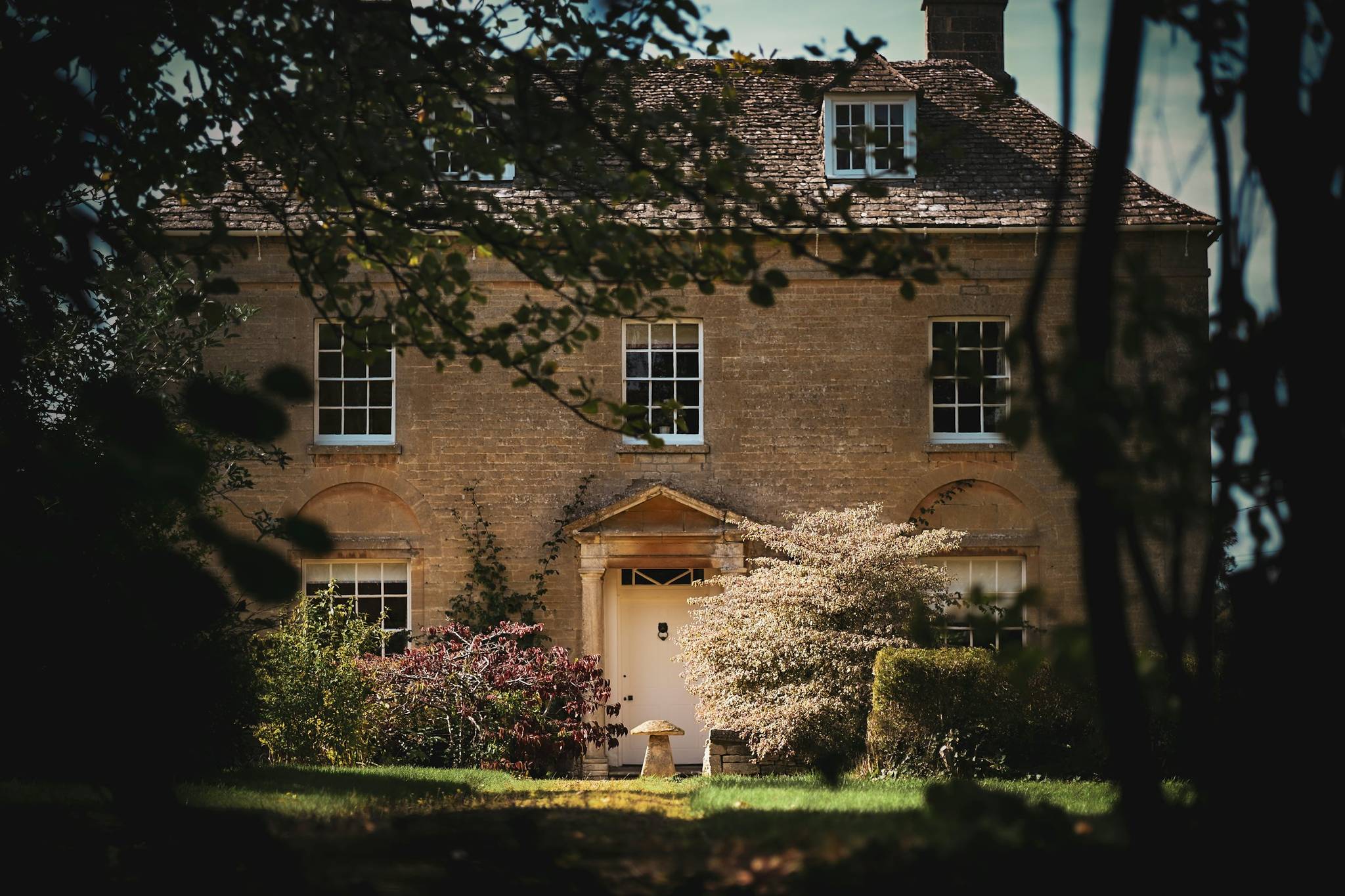 Stone house with a pale front door, seen through trees in soft sunlight